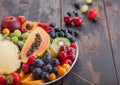 Fresh raw organic summer berries and exotic fruits in white plate on dark wooden background. Pineapple, papaya, grapes, nectarine Royalty Free Stock Photo