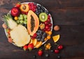 Fresh raw organic summer berries and exotic fruits in white plate on dark wooden background. Pineapple, papaya, grapes, nectarine Royalty Free Stock Photo