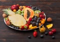 Fresh raw organic summer berries and exotic fruits in white plate on dark wooden background. Pineapple, papaya, grapes, nectarine Royalty Free Stock Photo