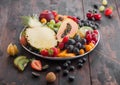 Fresh raw organic summer berries and exotic fruits in white plate on dark wooden background. Pineapple, papaya, grapes, nectarine Royalty Free Stock Photo