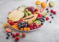 Fresh raw organic summer berries and exotic fruits in white plate on light background. Pineapple, papaya, grapes, nectarine, Royalty Free Stock Photo