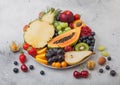 Fresh raw organic summer berries and exotic fruits in white plate on light background. Pineapple, papaya, grapes, nectarine, Royalty Free Stock Photo