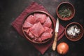 Fresh raw pieces of beef meat in a bowl with spices, herbs and onions on a dark background. Top view, flat lay, copy space Royalty Free Stock Photo