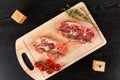 Fresh raw pork steaks with spices, tomatoes and thyme on a cutting kitchen board on a black wooden table. next to pepper s Royalty Free Stock Photo