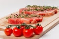 Fresh  raw pork steaks with spices, tomatoes and thyme on a cutting kitchen board on a white wooden table Royalty Free Stock Photo