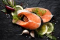 Fresh, raw salmon steaks with the addition of slices of lemon, garlic, onion, herbs and spices on a black stone background, top vi