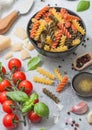 Fresh raw tricolore fusilli pasta in black bowl with cherry tomatoes and basil, garlic and oil with parmesan cheese on light Royalty Free Stock Photo