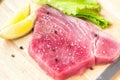 Fresh raw tuna fillet with black pepper corns, salt, lemon and olive oil on rustic background. Raw tuna steak on wooden cutboard,