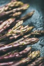 Fresh raw uncooked purple asparagus over dark background, vertical composition