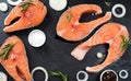 Fresh raw unprepared fish salmon or trout, steaks, in a skillet for cooking, with salt, pepper On black stone concrete table, copy