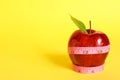 Fresh red apple with measuring tape on yellow background. Space for text Royalty Free Stock Photo