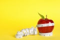 Fresh red apple with measuring tape on yellow background. Space for text Royalty Free Stock Photo