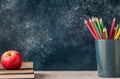 Fresh red apple sits on stacked notebooks in a classroom with colorful pencils in background Royalty Free Stock Photo