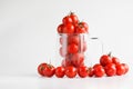 Fresh red baby plum or cherry tomatoes next to and inside a transparent mug. The concept of making tomato juice. White background Royalty Free Stock Photo