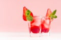 Fresh red fruit cocktail with ice cubes, strawberry slice, green mint in elegant misted shot glasses on soft light pink color. Royalty Free Stock Photo