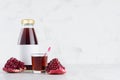 Fresh red garnet juice in glass bottle mock up with blank label, straw, wine glass, fruit piece on white wood table in light.