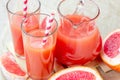 Fresh red grapefruit juice in a glass with a straw and jar with fruit pieces on light wooden background. Royalty Free Stock Photo