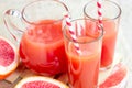 Fresh red grapefruit juice in a glass with a straw and jar with fruit pieces on light wooden background. Royalty Free Stock Photo