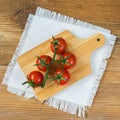 Fresh red ripe tomatoes cherry with water drops on branch on wooden background with rustic chopping board in center Royalty Free Stock Photo