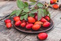 Fresh red rose hips and green leaves on a bowl on a wooden table Royalty Free Stock Photo