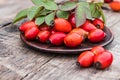 Fresh red rose hips and green leaves on a bowl on a wooden table Royalty Free Stock Photo