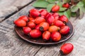 Fresh red rose hips and green leaves on a bowl on a wooden table Royalty Free Stock Photo