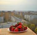 Fresh red strawberries on a white plate stands on a bamboo napkin against the background of the blurry panorama of the spring