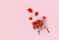 Fresh strawberry in shopping cart on pink background. Online shopping and Valentines Day minimalistic concept.