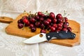 Folding knife cutting edge black handle fresh red sweet cherry vegetarian natural product brown wooden plate background Royalty Free Stock Photo