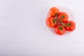 Fresh red tomatoes on a white plate at a white table shot from the top Royalty Free Stock Photo