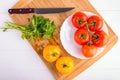 Fresh red and yellow tomatoes from above on a wooden board with a knife in a white plate at a white table Royalty Free Stock Photo