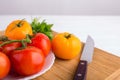 Fresh red and yellow tomatoes close up on a wooden board with a knife at a white table Royalty Free Stock Photo