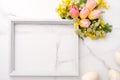 Fresh red and yellow tulips flowers bouquet, blank photo frame and eggs on white wooden background on white marble background. Spr Royalty Free Stock Photo