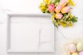 Fresh red and yellow tulips flowers bouquet, blank photo frame and eggs on white wooden background on white marble background. Spr Royalty Free Stock Photo