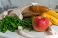 Fresh ripe apple, bunch of parsley and green onion, bananas and French baguette in canvas reusable grocery tote bag on the kitchen