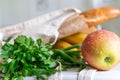 Fresh ripe apple, bunch of parsley and green onion, bananas and French baguette in canvas reusable grocery tote bag on the kitchen Royalty Free Stock Photo