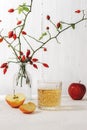 Fresh ripe apples and glass of apple juice or cider on white table. Vase with rosehip branches on the background. Autumn Royalty Free Stock Photo