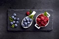 Fresh ripe berry in white bowl on black background. Raspberry and blueberry on black stone