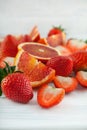 Fresh ripe blood oranges and strawberries, slices, rustic food photography on white wood plate