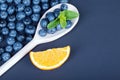 Fresh and ripe blueberries in a wooden spoon. A heap of organic berries and juicy citrus on a dark blue background. Royalty Free Stock Photo