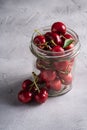 Fresh ripe cherry branch near to cherries with green leaves in glass jar, summer vitamin berries on grey stone background Royalty Free Stock Photo