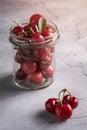 Fresh ripe cherry branch near to cherries with green leaves in glass jar, summer vitamin berries on grey stone background Royalty Free Stock Photo