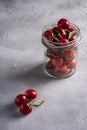 Fresh ripe cherry branch near to cherries with green leaves in glass jar, summer vitamin berries on grey stone background Royalty Free Stock Photo