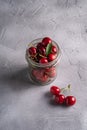 Fresh ripe cherry branch near to cherries with green leaves in glass jar, summer vitamin berries on grey stone background Royalty Free Stock Photo