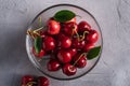 Fresh ripe cherry fruits with green leaves in glass bowl, summer vitamin berries on grey stone background Royalty Free Stock Photo