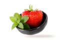 Fresh ripe garden large strawberry berry and mint leaves in a dark ceramic bowl flying isolated on white