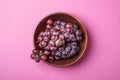 Fresh ripe grape berries in brown wooden bowl on pink minimal background