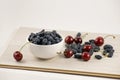 Fresh ripe honeysuckle berries and cherry in a ceramic bowl on a wooden board. Healthy breakfast. White bowl of honeysuckle. Royalty Free Stock Photo