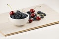 Fresh ripe honeysuckle berries and cherry in a ceramic bowl on a wooden board. Healthy breakfast. White bowl of honeysuckle. Royalty Free Stock Photo