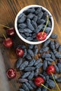 Fresh ripe honeysuckle berries and cherry in a ceramic bowl on a wooden board. Healthy breakfast. White bowl of honeysuckle. Royalty Free Stock Photo